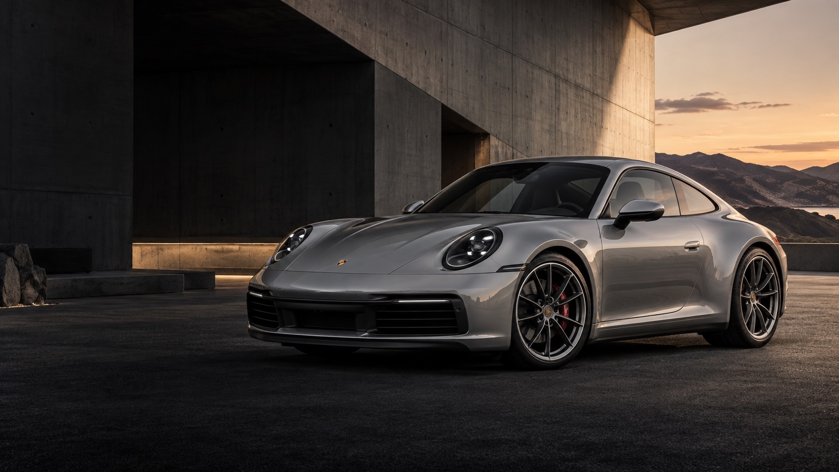 Серебристый Porsche 911 на фоне монументальной архитектуры на закате